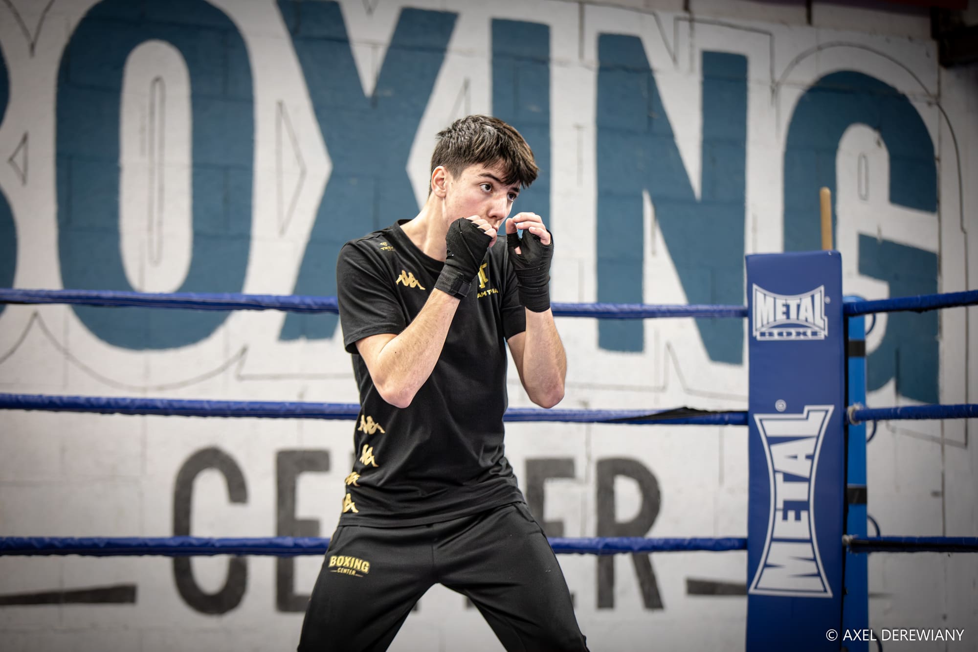 Un boxeur en garde devant le mot « Boxing Center » peint sur le mur bleu de la salle.